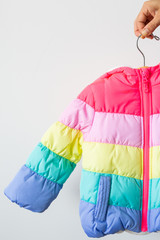 Woman holding rainbow toddlers puffer jacket on hanger, white background