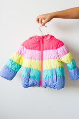 Woman holding rainbow toddlers puffer jacket on hanger, white background