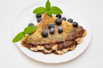 homemade crepes with chocolate cream, banana and blueberries on white background. pancakes