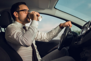 Businessman driving a car while drinking coffee
