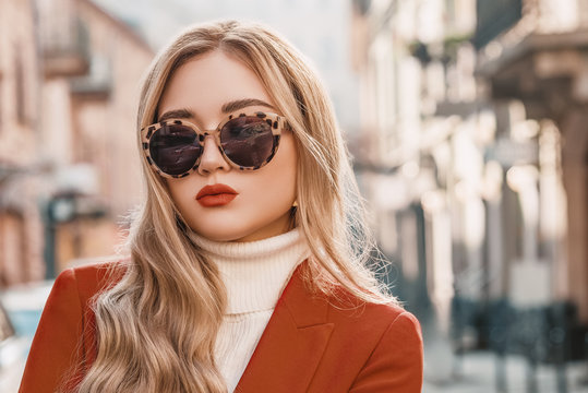 Outdoor close up street fashion portrait of young elegant lady with terracotta color lips makeup, wearing trendy turtle frame sunglasses, blazer, white classic turtleneck. Copy, empty space for text