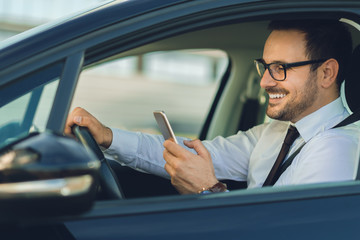 Smiling businessman using smart phone while driving a car