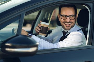 Smiling businessman driving a car while drinking coffee