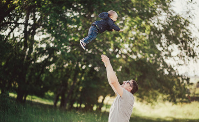 Happy father playing with his little son in a green park.