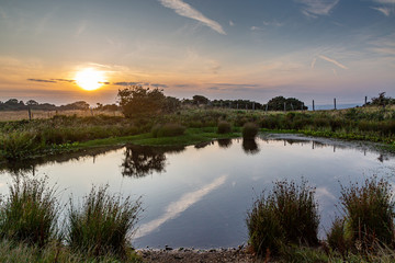 Naklejka na ściany i meble Burnt House dew pond at Ditchling Beacon, with a sunset sky behind