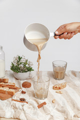 Girl pours coffee with milk in a glass cup. Arrangement of glasses with coffee, flowers and cookies.
