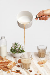 Girl pours coffee with milk in a glass cup. Arrangement of glasses with coffee, flowers and cookies.
