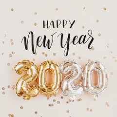 Happy New year 2020 celebration. Gold and silver foil balloons numeral 2020 and confetti on pink...