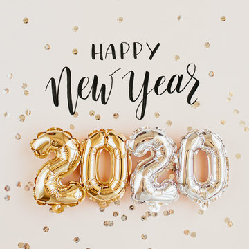Happy New year 2020 celebration. Gold and silver foil balloons numeral 2020 and confetti on pink background. Flat lay