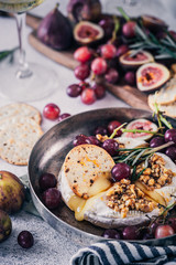 Fancy baked brie cheese platter with honey and walnuts, fresh rosemary. Red grapes, figs and white wine