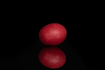 One whole red sugared nut dragee isolated on black glass