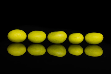 Group of five whole yellow sugared nut dragee isolated on black glass