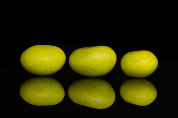 Group of three whole yellow sugared nut dragee isolated on black glass