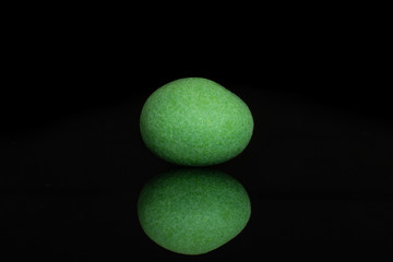 One whole green sugared nut dragee isolated on black glass