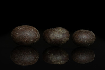 Group of three whole brown sugared nut dragee isolated on black glass