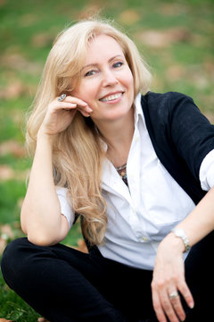 A close-up portrait of Caucasian woman with long blond hair looking strait to the camera, smiling