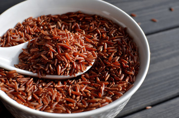 red rice in a ceramic bowl with spoon against dark wooden background