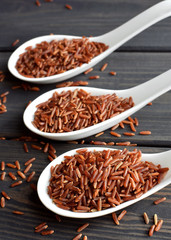 Red rice in ceramic spoons on dark wooden background