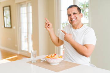 Middle age man eating rice at home smiling and looking at the camera pointing with two hands and fingers to the side.