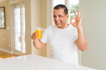 Fototapeta premium Middle age man drinking a glass of orange juice at home doing ok sign with fingers, excellent symbol