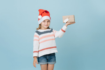 Portrait of cute little first grader girl in a santa's hat holding present
