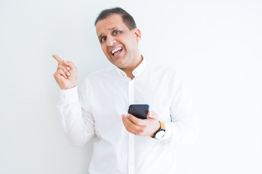 Middle age man using smartphone over white wall very happy pointing with hand and finger to the side