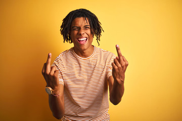 Afro man with dreadlocks wearing striped t-shirt standing over isolated yellow background Showing...