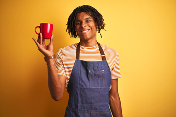 Afro barista man with dreadlocks drinking cup of coffee over isolated yellow background with a happy face standing and smiling with a confident smile showing teeth