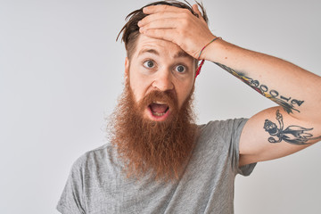 Young redhead irish man wearing t-shirt standing over isolated grey background stressed with hand on head, shocked with shame and surprise face, angry and frustrated. Fear and upset for mistake.