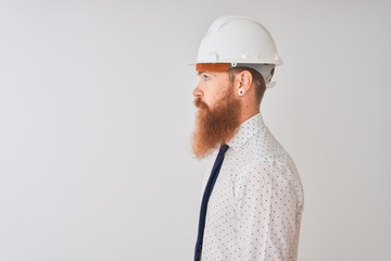 Young redhead irish architect man wearing security helmet over isolated white background looking to side, relax profile pose with natural face with confident smile.