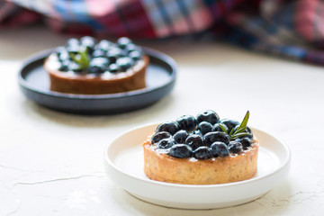 Delicious blueberry tartlets with vanilla custard cream on a black and white plates on white table. Front view. 