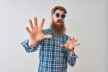 Young redhead irish man wearing casual shirt and sunglasses over isolated white background afraid and terrified with fear expression stop gesture with hands, shouting in shock. Panic concept.