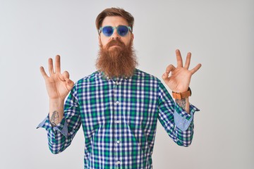 Young redhead irish man wearing casual shirt and sunglasses over isolated white background relax and smiling with eyes closed doing meditation gesture with fingers. Yoga concept.
