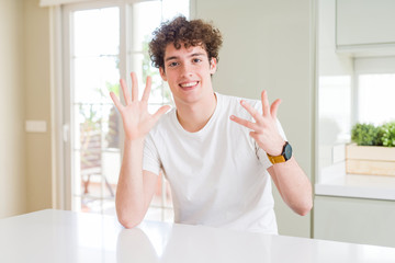 Young handsome man wearing white t-shirt at home showing and pointing up with fingers number nine...