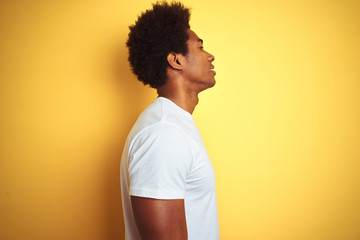 American man with afro hair wearing white t-shirt standing over isolated yellow background looking...