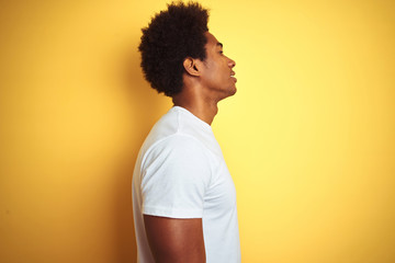 American man with afro hair wearing white t-shirt standing over isolated yellow background looking to side, relax profile pose with natural face with confident smile.