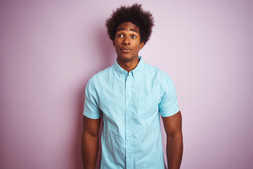 Young american man with afro hair wearing blue shirt standing over isolated pink background smiling looking to the side and staring away thinking.