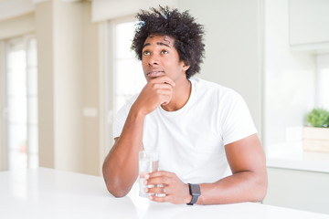 African American man drinking a glass of water at home serious face thinking about question, very confused idea