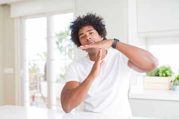 Young african american man wearing casual white t-shirt sitting at home Doing time out gesture with hands, frustrated and serious face