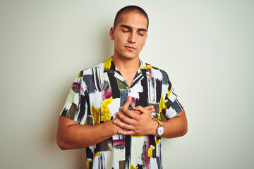 Young handsome man wearing summer shirt over white isolated background smiling with hands on chest with closed eyes and grateful gesture on face. Health concept.