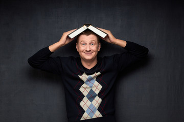Portrait of funny man holding big opened book on his head