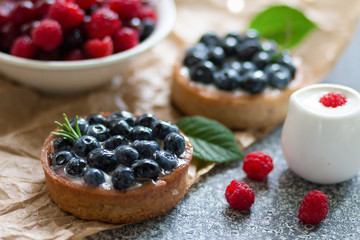 Tartalets with blueberry berries, plate with fresh raspberry and dairy with sour cream on the grey surface. 