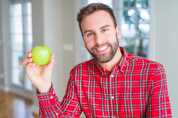 Handsome man eating fresh healthy green apple with a happy face standing and smiling with a confident smile showing teeth