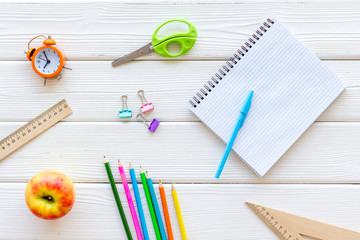 Student's desk with stationery, apple, alarm clock, textbook on white wooden background top view