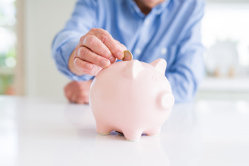 Close up of man putting a coin inside of piggy bank as savings