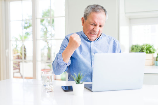Handsome senior man using computer laptop working on internet annoyed and frustrated shouting with anger, crazy and yelling with raised hand, anger concept
