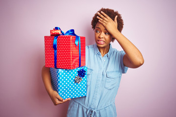 African american woman holding birthday gifts over pink isolated background stressed with hand on head, shocked with shame and surprise face, angry and frustrated. Fear and upset for mistake.