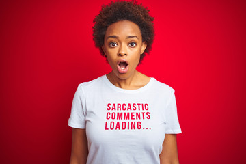 African american woman wearing sarcastic comments t-shirt over red isolated background afraid and shocked with surprise expression, fear and excited face.