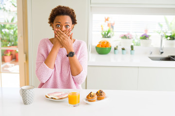 Obraz na płótnie Canvas Young african american woman eating breaksfast in the morning at home shocked covering mouth with hands for mistake. Secret concept.