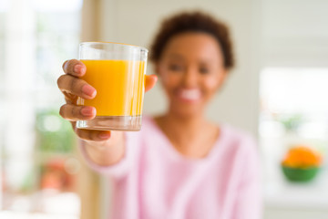 Young african american woman driking orange juice at home with a happy face standing and smiling...